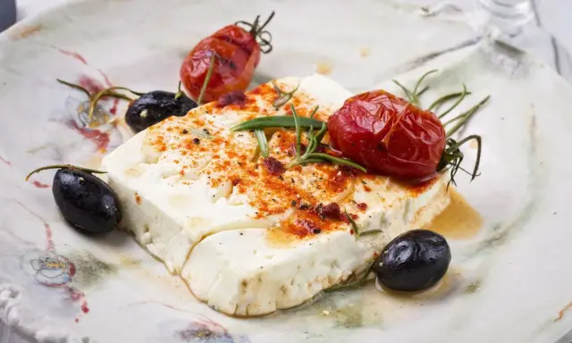 Feta al forno con pomodorini arrostiti, olive nere e rosmarino su un piatto rustico.