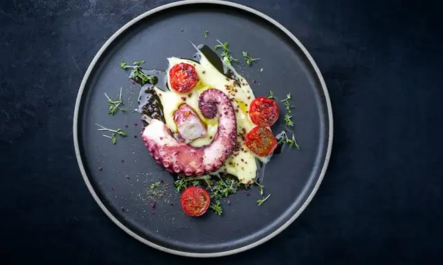 Un tentacolo di polpo alla griglia, servito su purè di patate con pomodorini confit e timo.