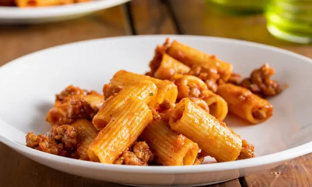 Rigatoni conditi con un ricco ragù di salsiccia alla napoletana, serviti su un piatto bianco.