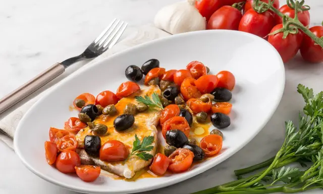 Un succulento pesce spada alla siciliana, condito con pomodorini, olive nere e capperi, guarnito con prezzemolo fresco.