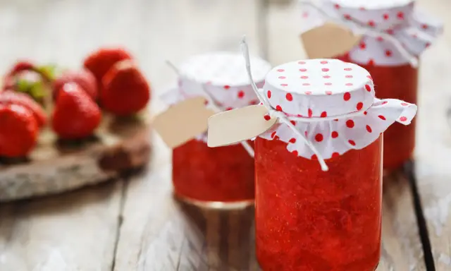 Barattoli di marmellata di fragole fatti in casa, con fragole fresche sullo sfondo.