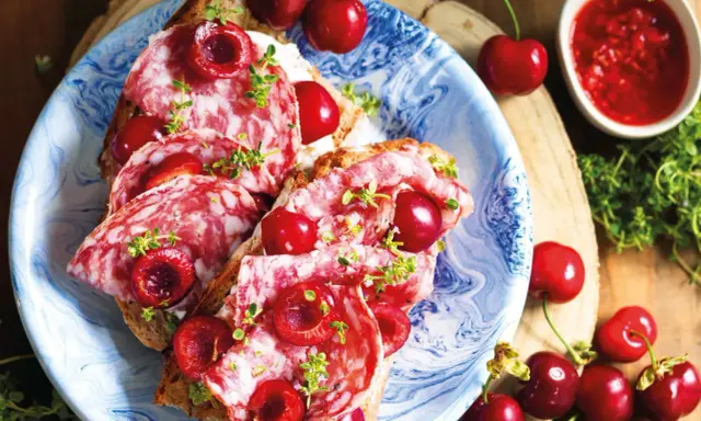 Bruschette con salame e varietà ciliegie giganti, guarnite con erbe aromatiche. Un connubio di sapori audace e invitante.