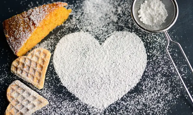 Un cuore di zucchero a velo, un pezzo di torta arancione e due biscotti a forma di cuore. Ecco come fare lo zucchero a velo per decorare dolci.
