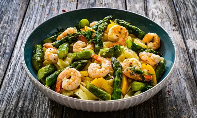 Un piatto invitante di pasta con asparagi e gamberetti, condito con erbe fresche e servito su un tavolo di legno rustico.