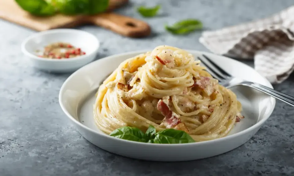 Un piatto di spaghetti alla carbonara, perfetto per la giornata della carbonara, guarnito con basilico fresco.