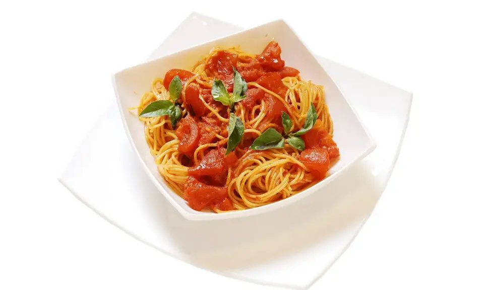 Un invitante piatto di spaghetti al pomodoro fresco, guarnito con foglie di basilico verde brillante.