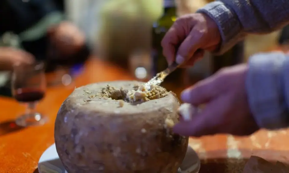 Un uomo serve un formaggio con i vermi, una specialità sarda, con un coltello. Sul tavolo, un bicchiere di vino rosso.