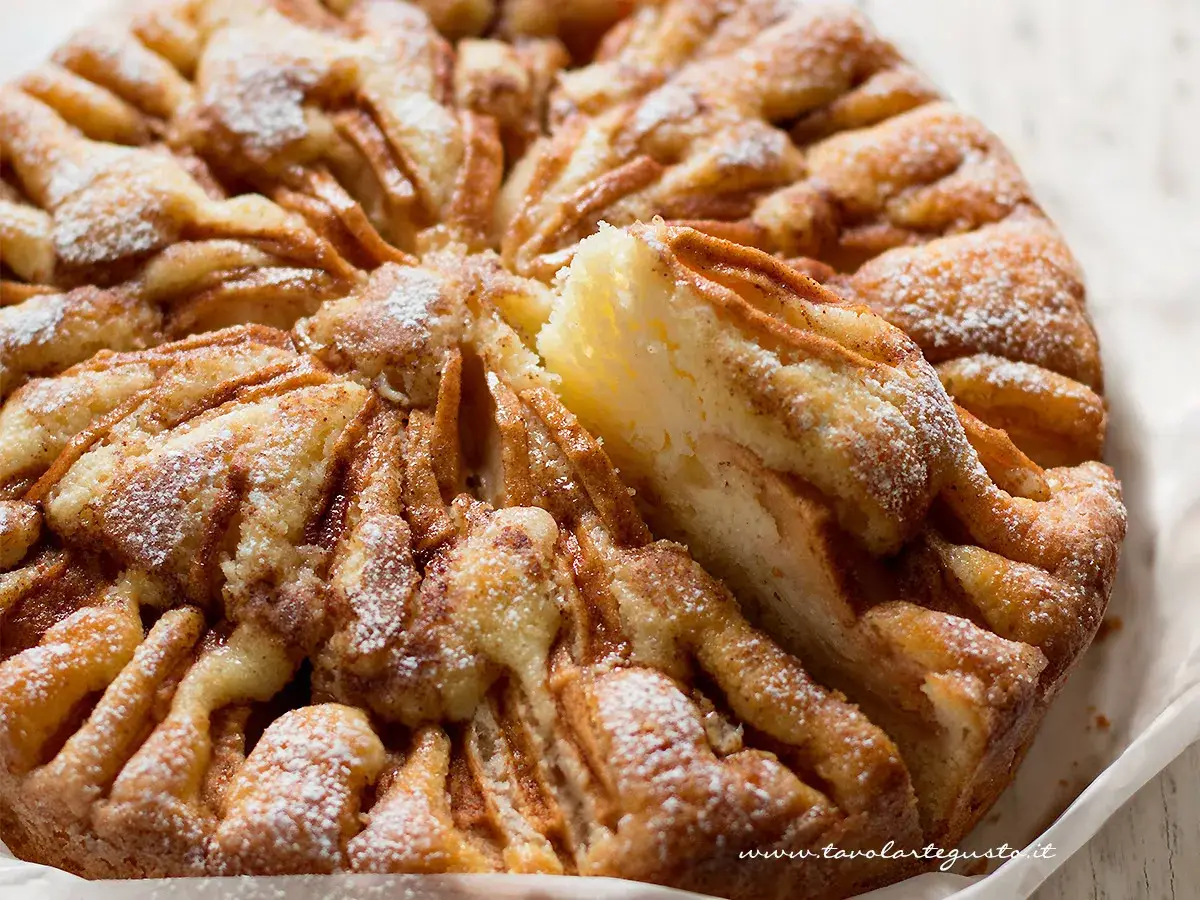 Una deliziosa torta di mele, cosparsa di zucchero a velo, con una fetta appena tolta che ne rivela la morbidezza.