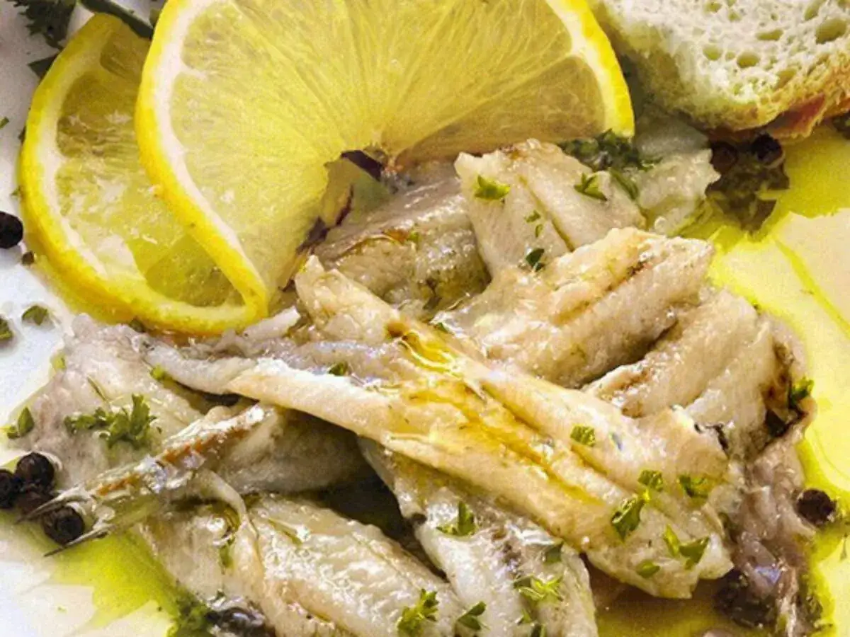 Alici in padella, succulente e profumate, con fette di limone e pane tostato. Un piatto semplice e gustoso.