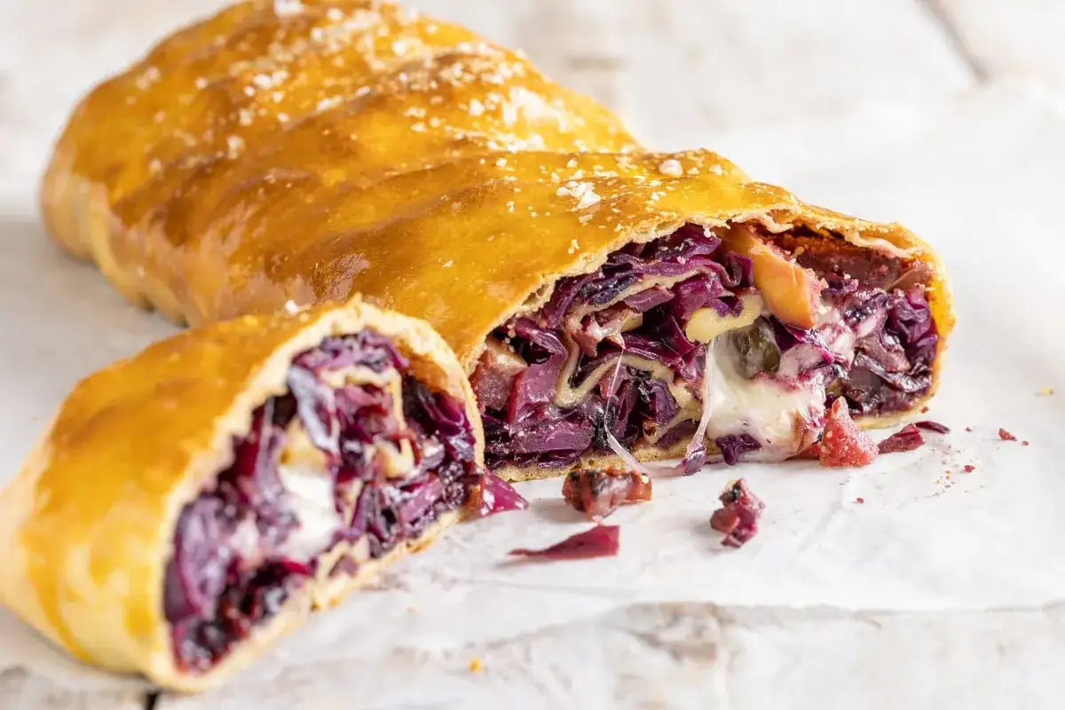 Strudel dorato ripieno di cavolo cappuccio rosso, mele e formaggio filante. Un sapore autunnale avvolgente.