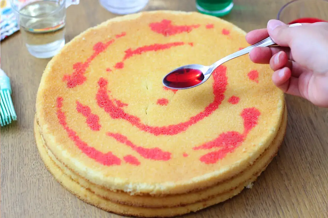 Un cucchiaino di sciroppo rosso viene versato su un pan di spagna decorato con un motivo a spirale. La bagna per pan di spagna render&agrave; la torta pi&ugrave; umida e gustosa.
