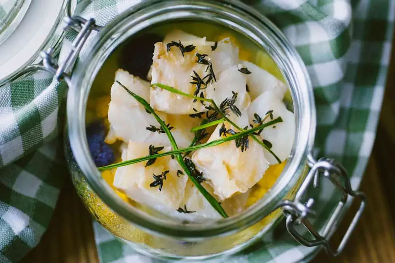 Pezzi di baccal&agrave; marinato in un barattolo di vetro, guarniti con erbe aromatiche. La differenza tra baccal&agrave; e stoccafisso &egrave; un tema culinario.