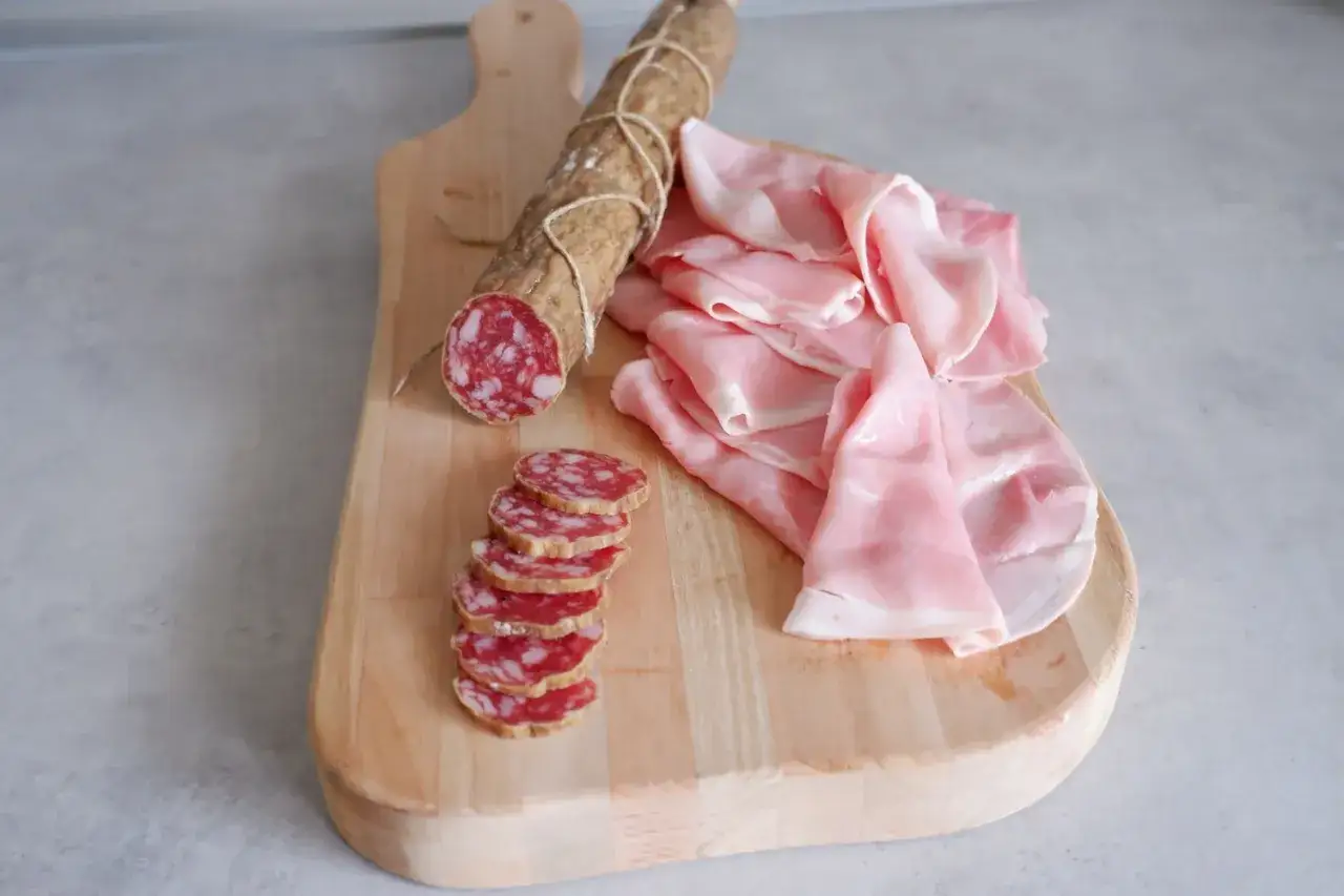 Tagliere in legno con salame affettato e fette di prosciutto cotto, un delizioso insaccato pronto per essere gustato.