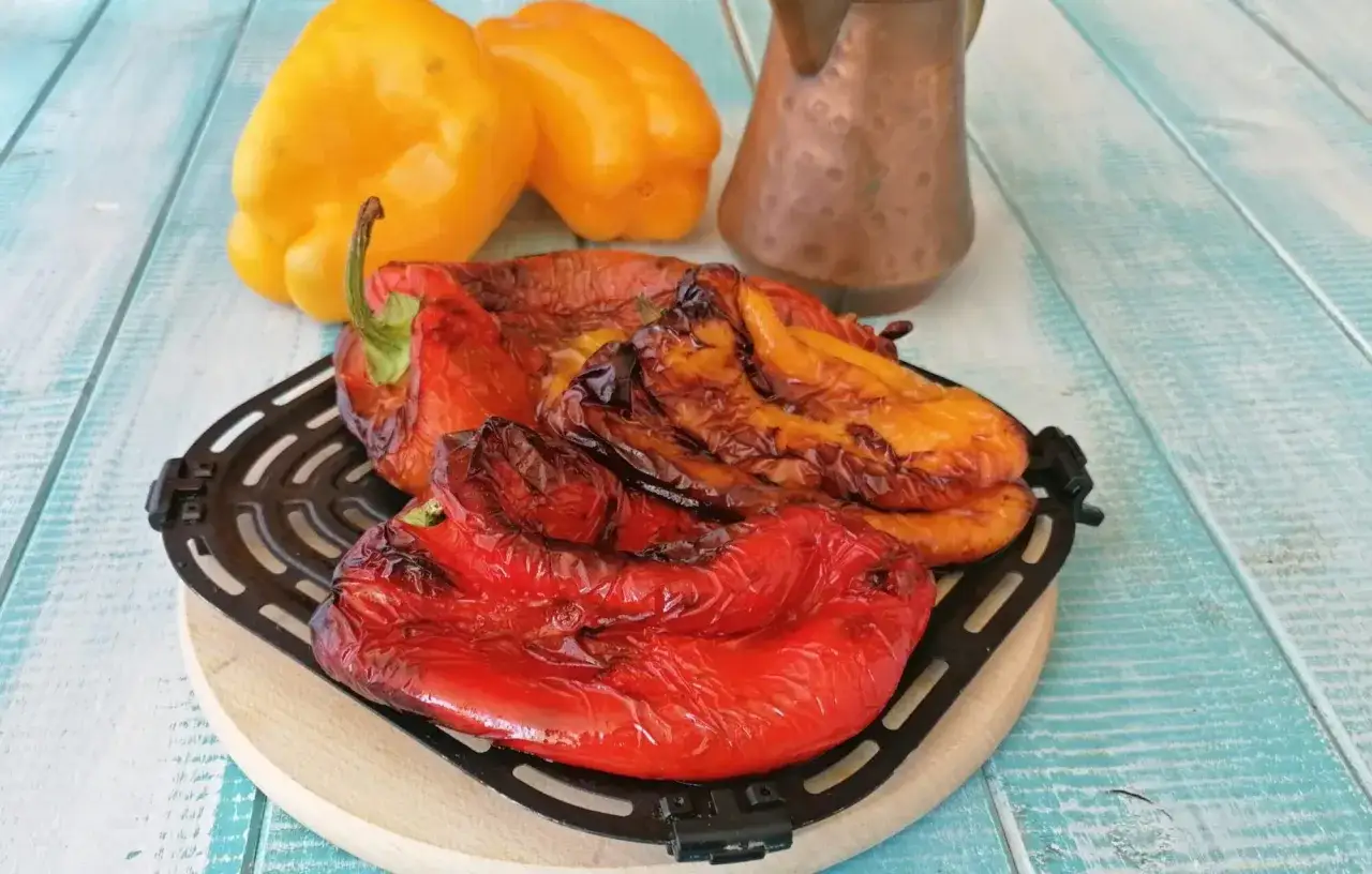 Peperoni rossi e gialli arrostiti nella friggitrice ad aria, con un pentolino di rame sullo sfondo.