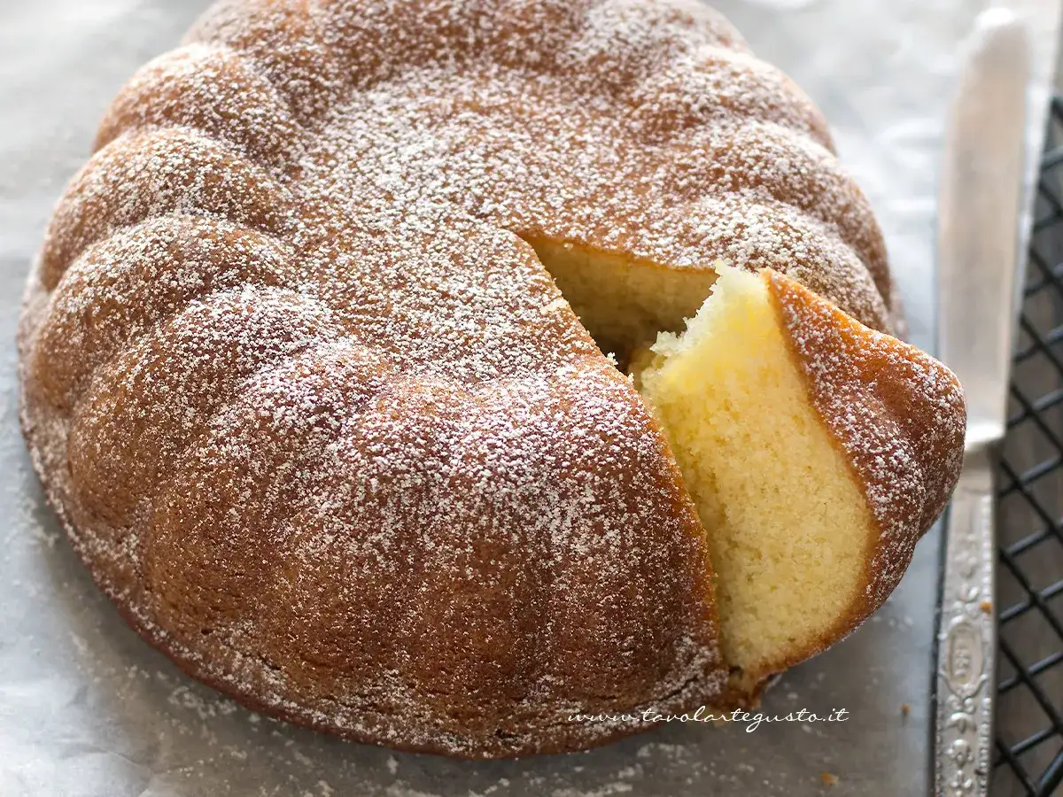 Torta 7 vasetti soffice e dorata, spolverata di zucchero a velo. Una fetta &egrave; stata tagliata, rivelando l'interno profumato.