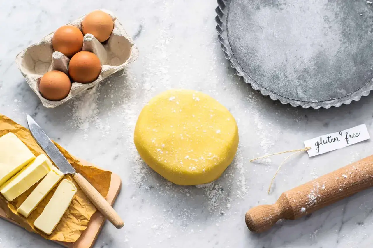 Impasto giallo per pasta frolla senza glutine, uova, burro e stampo per crostata pronti per creare dolci deliziosi.