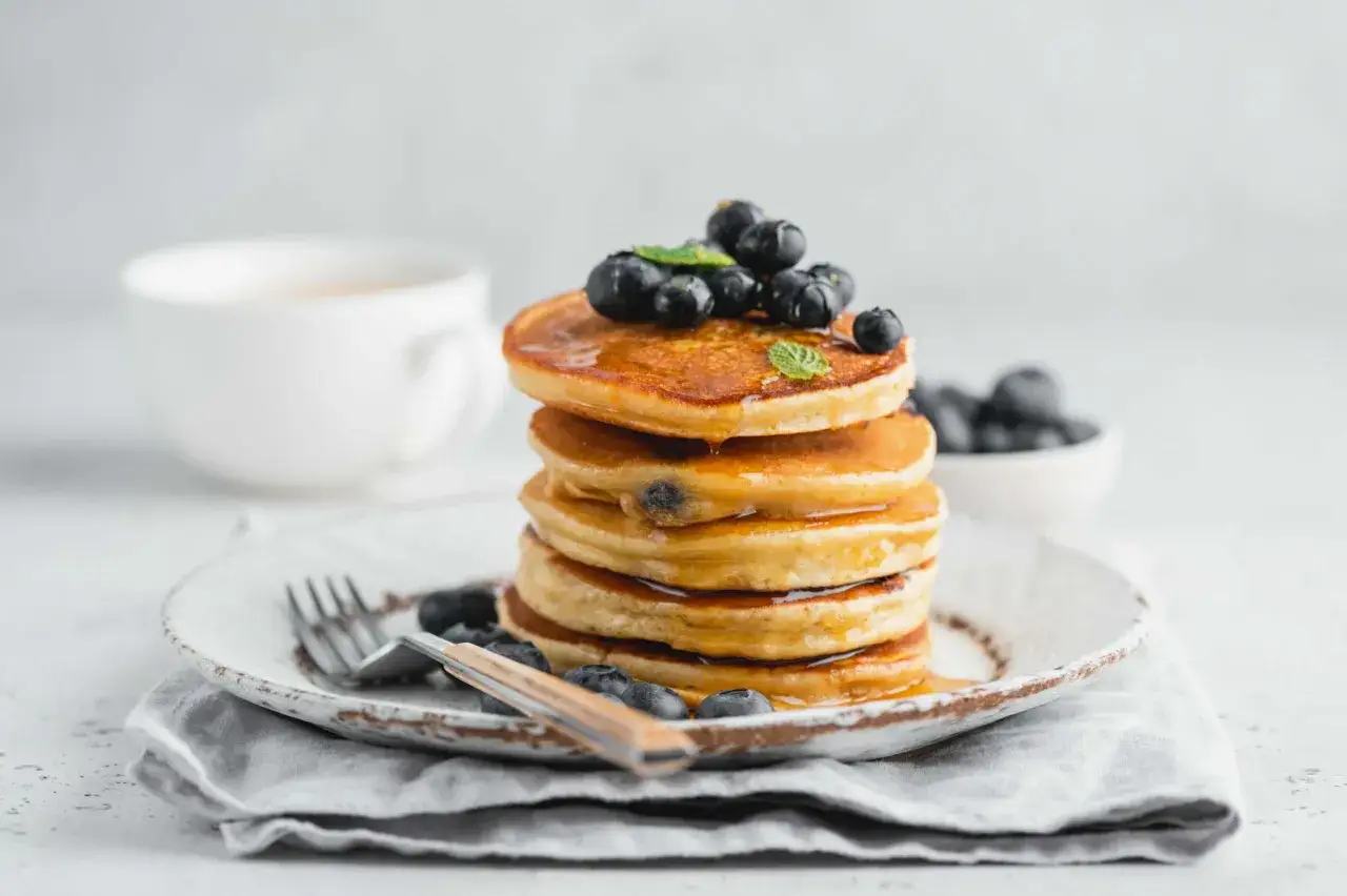 Pancake con farina di riso, guarniti con mirtilli freschi e sciroppo d'acero, pronti per una colazione deliziosa.