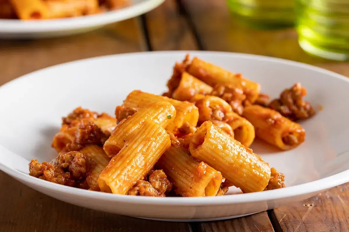 Rigatoni conditi con un ricco rag&ugrave; di salsiccia alla napoletana, serviti su un piatto bianco.