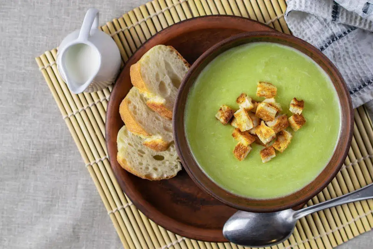 Vellutata di zucchine cremosa, guarnita con crostini dorati, accompagnata da pane fresco e una piccola brocca di latte.