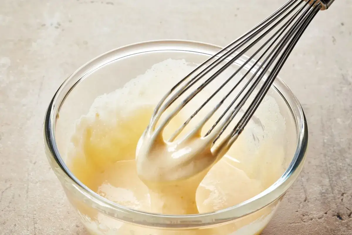 Frusta che monta una crema chiara in una ciotola di vetro, creando la base per una deliziosa pate a bombe.