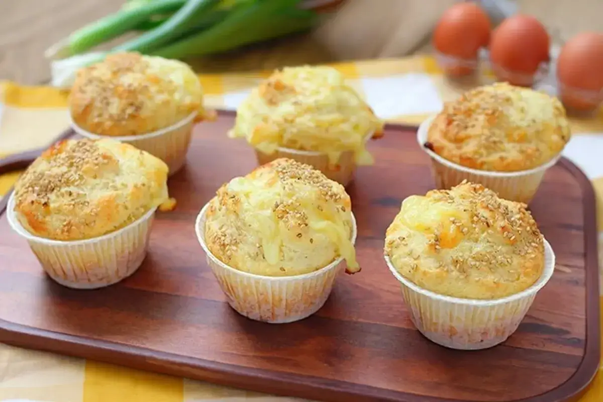 Sei muffin salati, perfetti per una ricetta muffin semplici, con formaggio fuso e semi di sesamo su un tagliere di legno.