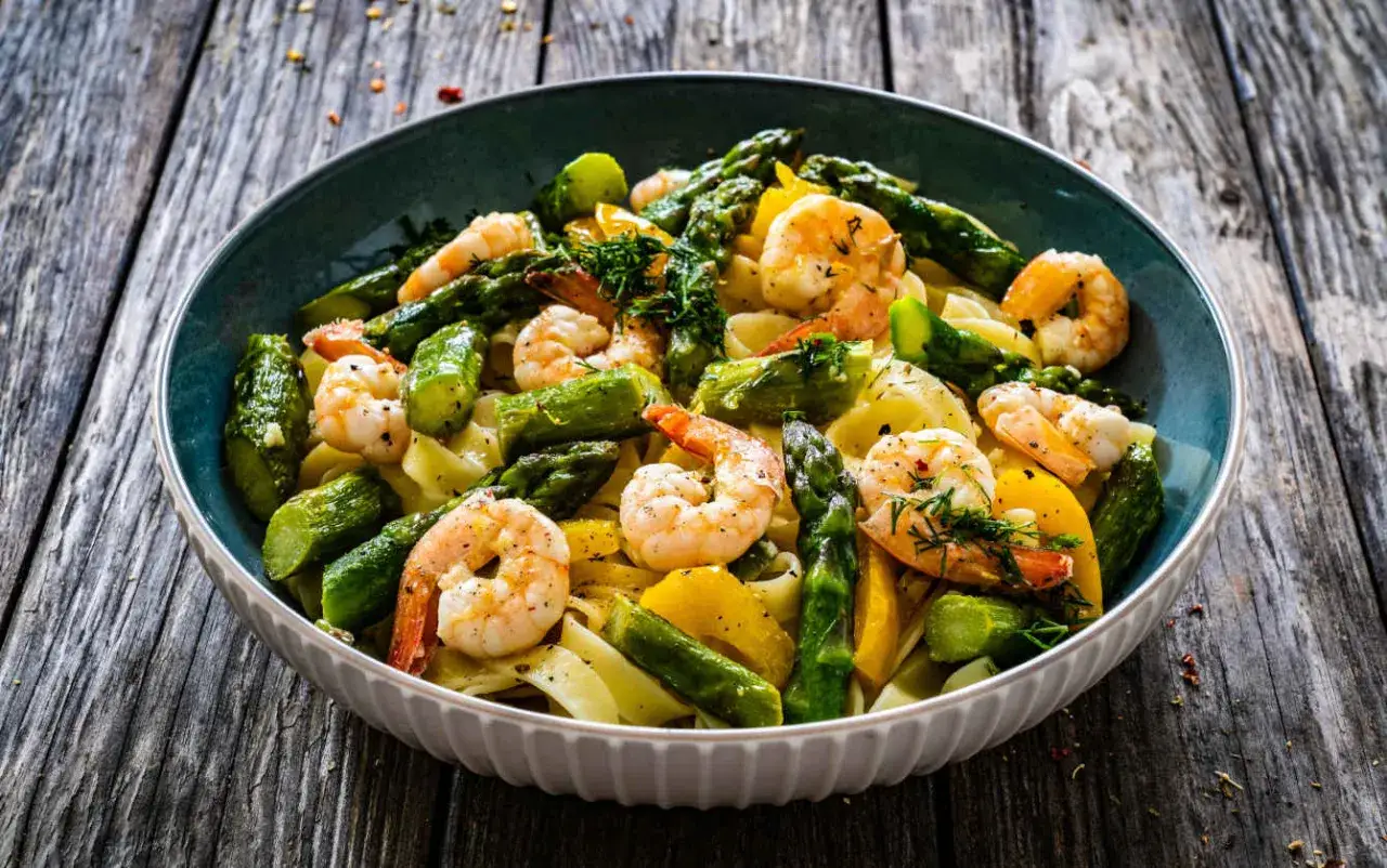 Un piatto invitante di pasta con asparagi e gamberetti, condito con erbe aromatiche fresche, su un tavolo di legno rustico.