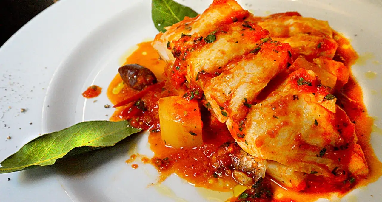 Un saporito baccal&agrave; alla romana con patate, pomodoro e olive, guarnito con foglie di alloro.
