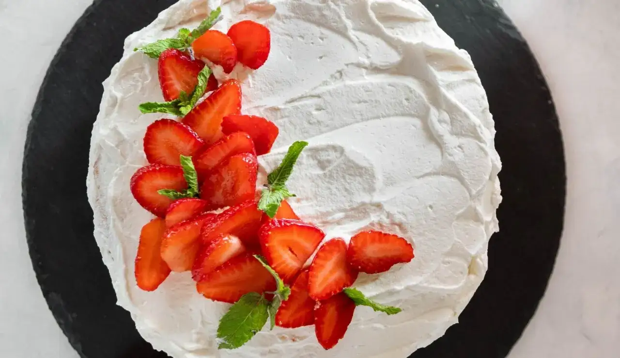 Deliziosa torta fragole e panna, decorata con fragole fresche affettate e foglie di menta, su una base scura.