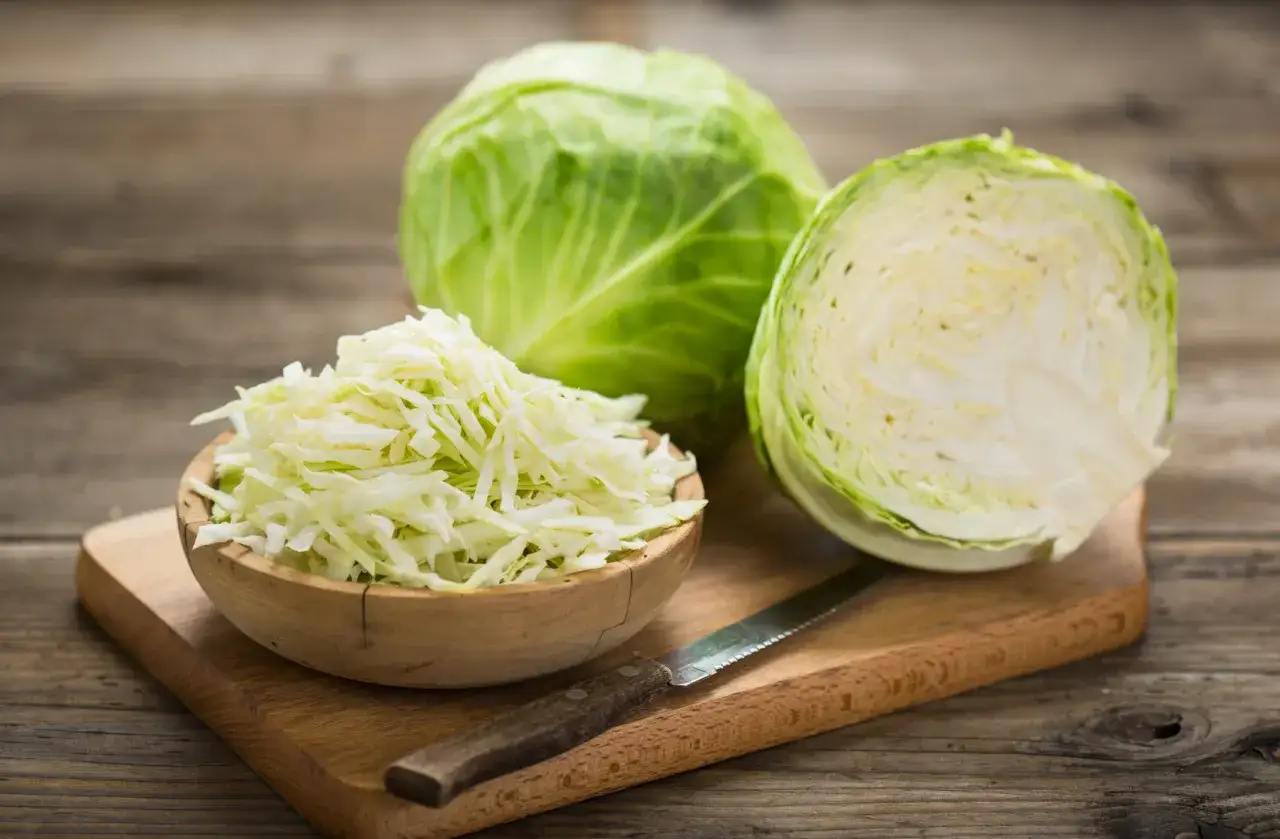 Verza tagliata finemente in una ciotola di legno, pronta per essere cucinata in padella. Accanto, una verza intera e una tagliata a met&agrave;.