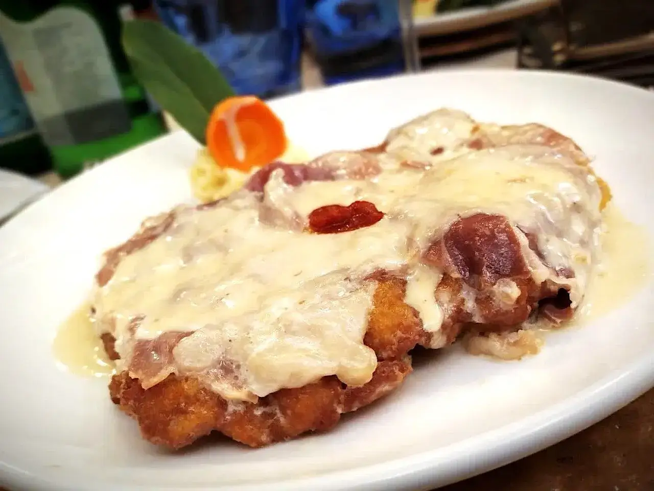 Cotoletta alla bolognese, dorata e filante, con prosciutto e formaggio fuso, servita su un piatto bianco.