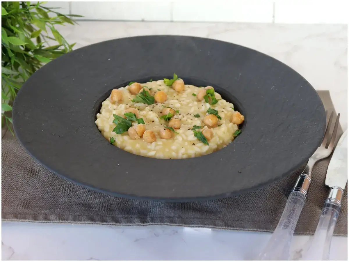Un cremoso risotto e ceci, guarnito con prezzemolo fresco e pepe nero, servito in un piatto scuro.
