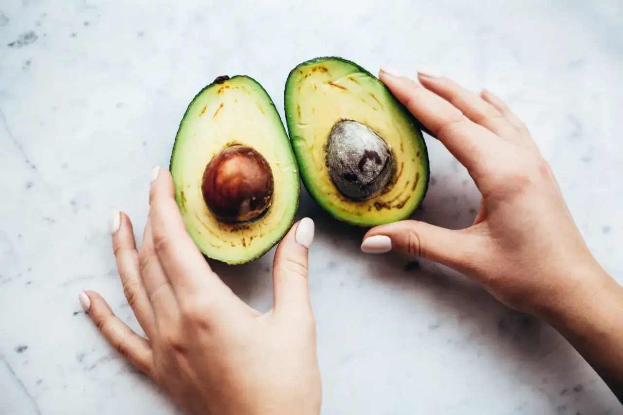 Due mani accarezzano un avocado tagliato a met&agrave;, mostrando come si mangia l'avocado: un frutto cremoso pronto per essere gustato.