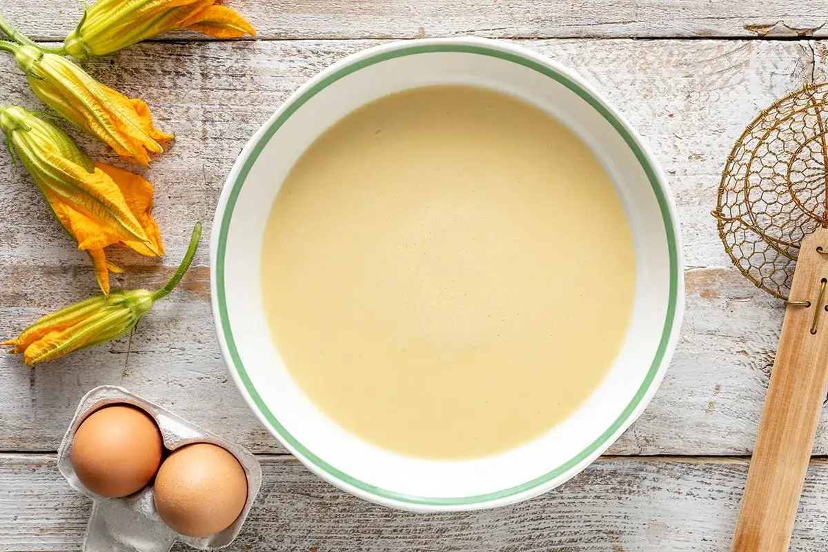 Ciotola con pastella per fiori di zucca, uova e fiori freschi pronti per essere fritti.