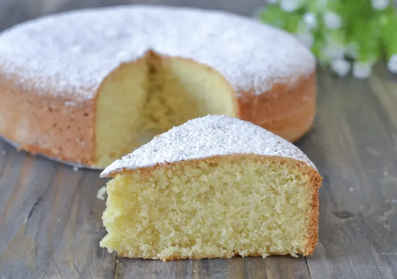 Una fetta di torta soffice con farina di mandorle, cosparsa di zucchero a velo, su un tavolo di legno.