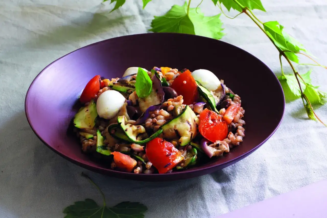 Insalata di farro estiva con verdure grigliate, pomodorini, mozzarelline e basilico, un piatto fresco e colorato.