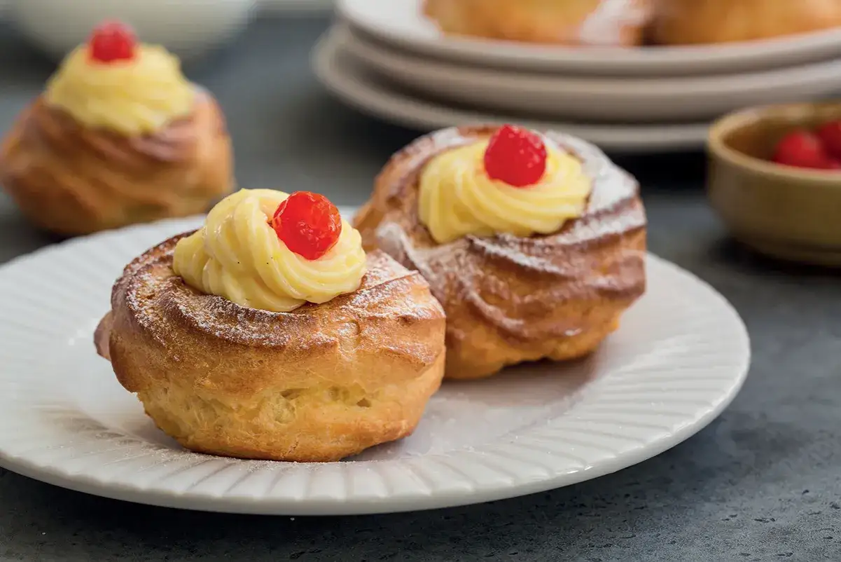 Zeppole di San Giuseppe, dolci fritti con crema pasticcera e ciliegina rossa, spolverati di zucchero a velo.