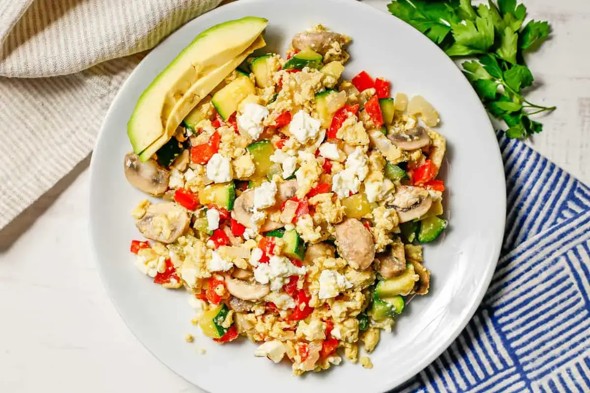 Uova strapazzate con verdure e feta, un piatto salutare che risponde alla domanda: quante uova a settimana? Accompagnato da avocado fresco.