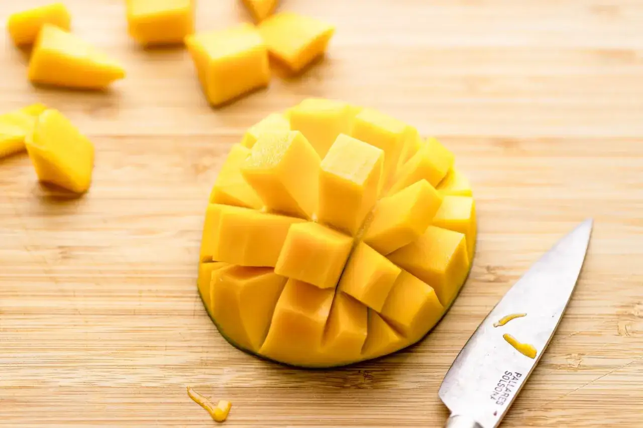 Ecco come si mangia il mango: un frutto tagliato a cubetti su un tagliere di legno, pronto per essere gustato.