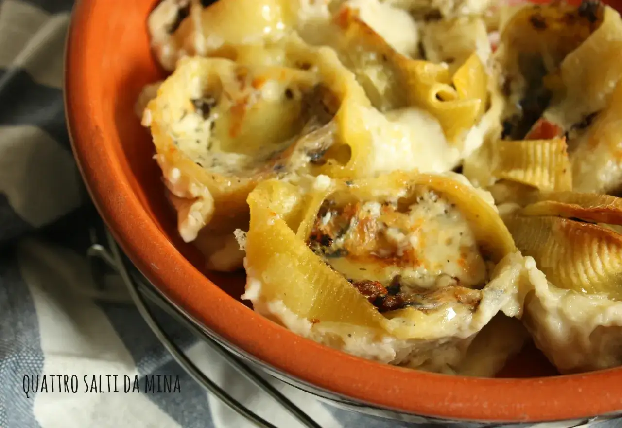 Conchiglioni ripieni al forno, dorati e filanti, in una terrina arancione. Un piatto invitante e gustoso.