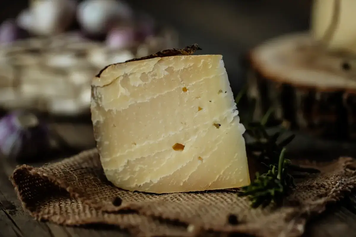 Un pezzo di formaggio stagionato su tela grezza, con aglio e rosmarino sullo sfondo. Ideale per chi cerca formaggi in gravidanza sicuri e gustosi.