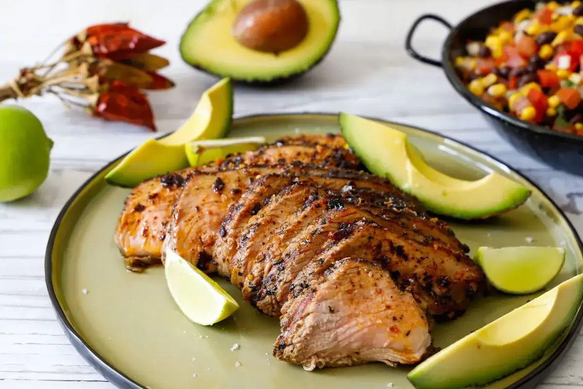 Fette di codone di manzo succulento, servite con spicchi di lime e avocado. Un piatto saporito e invitante.