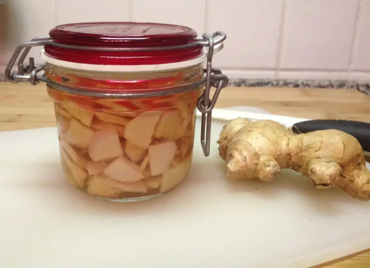 Barattolo con zenzero sott'aceto e radice fresca accanto. Scopri zenzero come si mangia, un ingrediente versatile per piatti piccanti e digestivi.