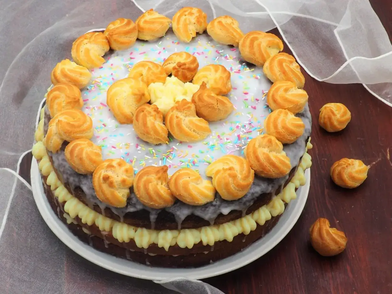 Torta decorata con bign&egrave; e crema al latte, spolverata di codette colorate.