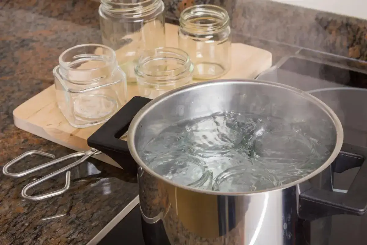 Vasi di vetro immersi in acqua bollente per sterilizzarli. Pinze per vasi pronte all'uso.