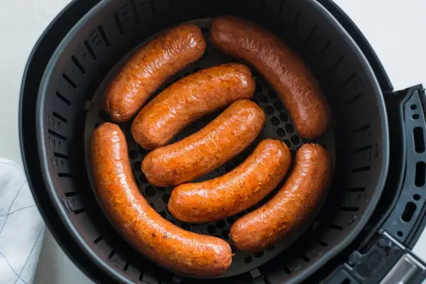 Sette salsicce dorate e succulente cuociono nella friggitrice ad aria, pronte per essere gustate.