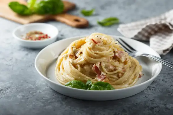 Un piatto di spaghetti alla carbonara, perfetto per la giornata della carbonara, guarnito con basilico fresco.