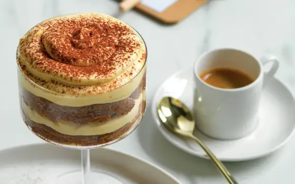 Delizioso tiramisù senza caffè, stratificato con crema e cacao, accanto a un espresso.