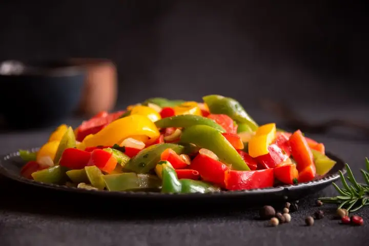 Peperoni colorati, cotti alla perfezione nella friggitrice ad aria, serviti su un piatto scuro. Un contorno sano e gustoso.
