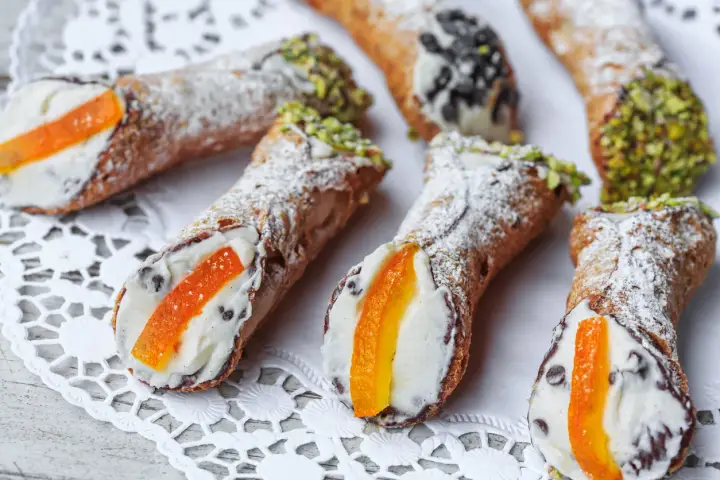 Cannoli siciliani, dolci tipici con crema e canditi, spolverati di zucchero a velo e guarniti con pistacchi o gocce di cioccolato.