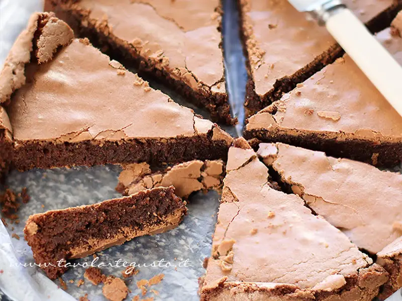 Una deliziosa torta tenerina al cioccolato, tagliata a fette triangolari, mostra la sua crosta croccante e il cuore morbido.